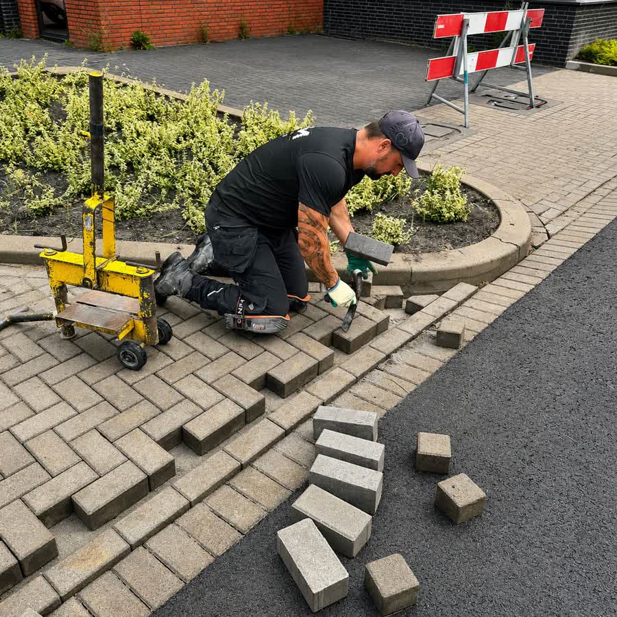 Stratenmaker past betonstraatstenen in langs een border